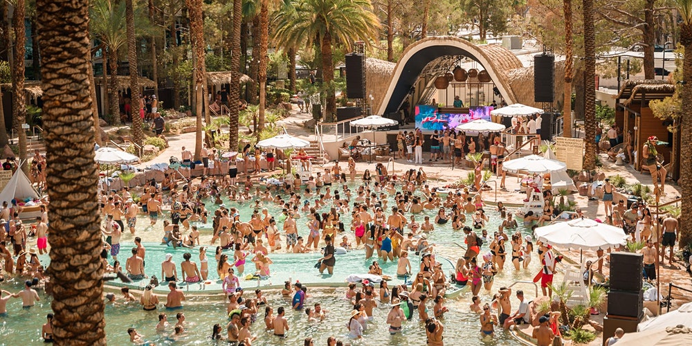 Packed Las Vegas dayclub pool party with DJ stage and palm trees