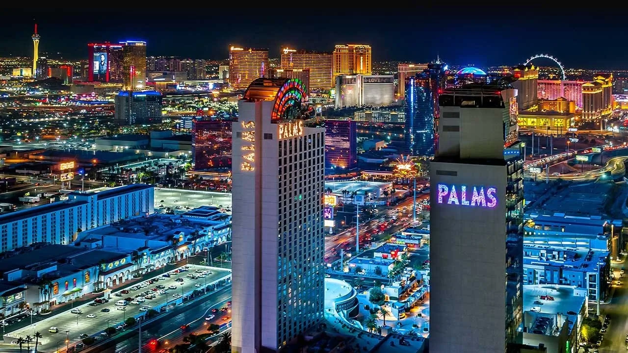 The Palms towers lit up at night with the Las Vegas Strip skyline behind them