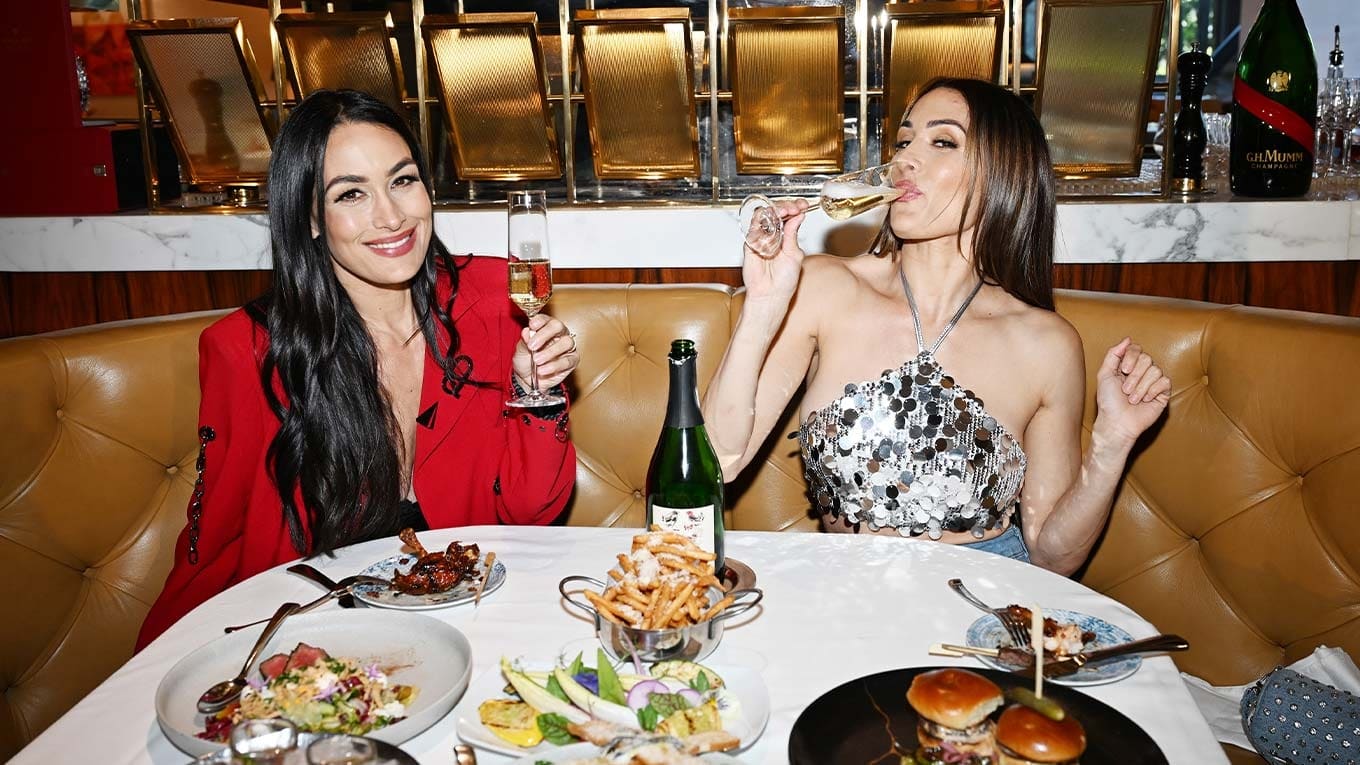 Two guests with champagne in a tufted leather booth surrounded by shared plates