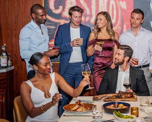 A group of guests with cocktails and wine beside the casino neon artwork