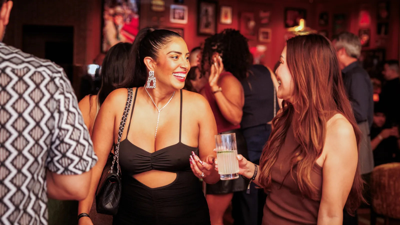 Two women talking and laughing over cocktails in the warm red light of Vinyl Room Las Vegas