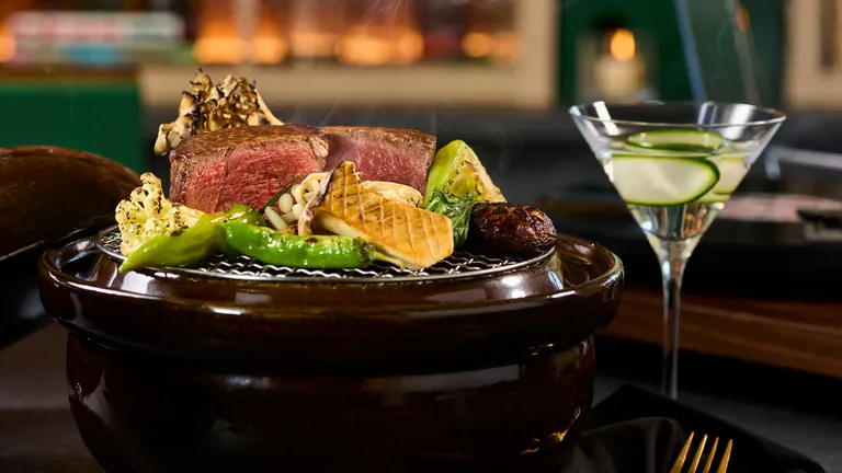 Japanese Kobe beef served over a grill set into a clay pot, next to a cucumber martini