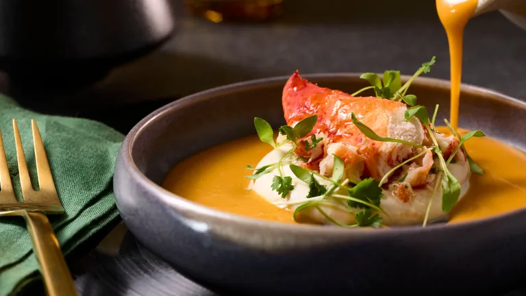 Lobster tail over whipped coconut tofu with a warm coconut broth being poured into the bowl