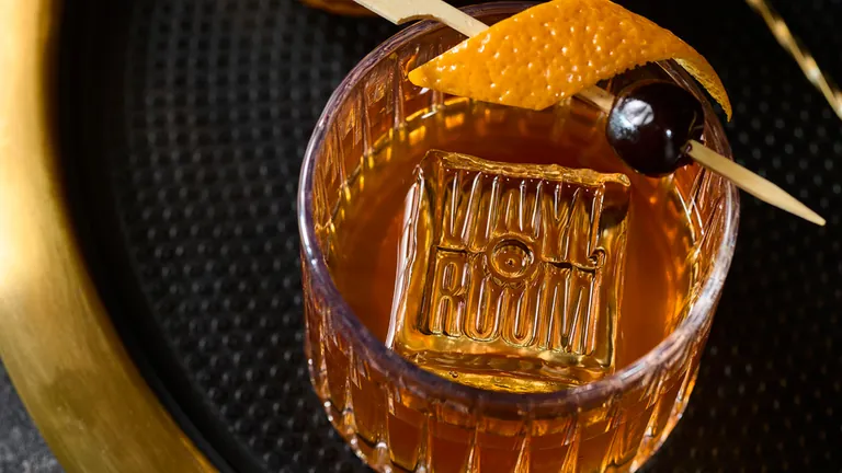 Old fashioned cocktail on a gold tray with a Vinyl Room branded ice cube, orange peel and cherry