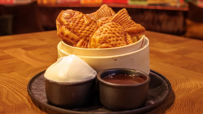 Fish-shaped taiyaki pastries in a bamboo steamer with cream and chocolate dipping sauces
