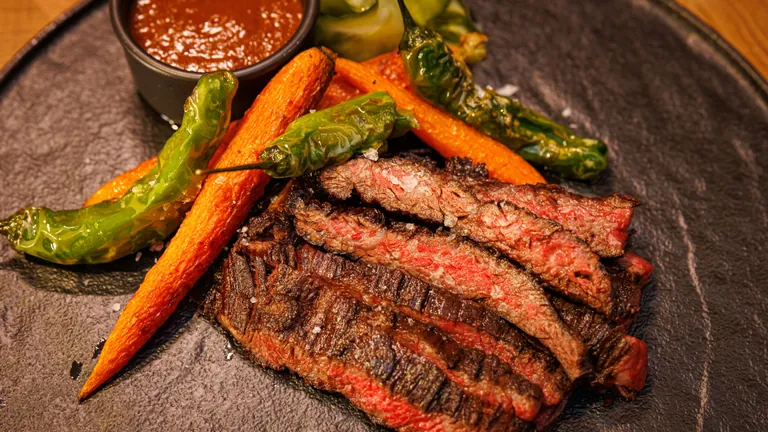 Sliced wagyu skirt steak with charred carrots, blistered shishito peppers and a pot of gochujang steak sauce